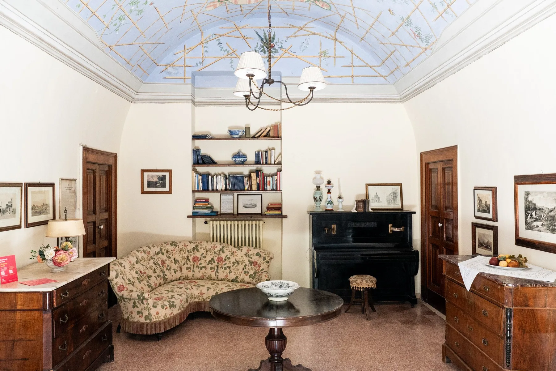 Una sala amueblada con un sofá estampado y un piano negro bajo un techo pintado.