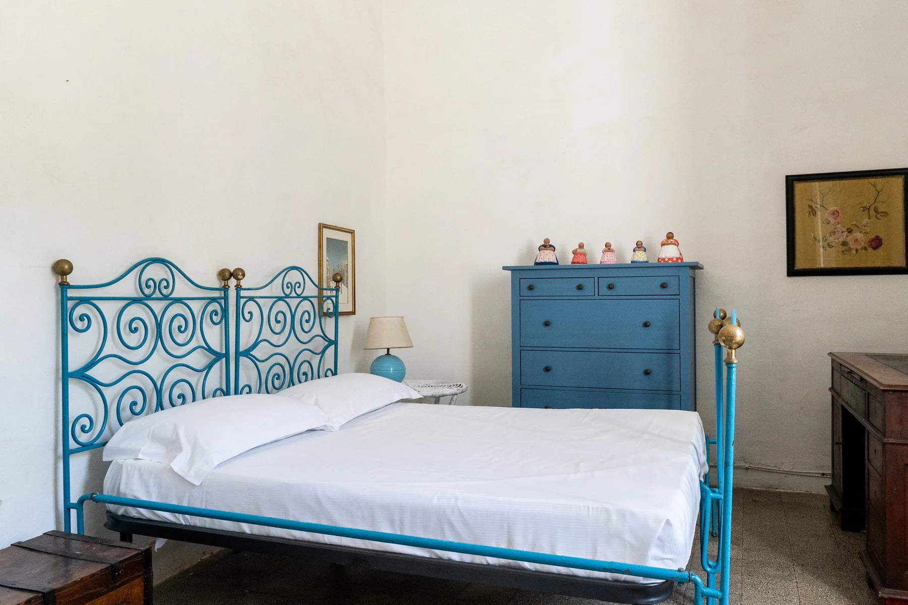 Un dormitorio con una cama blanca, estructura metálica azul y cómoda azul.