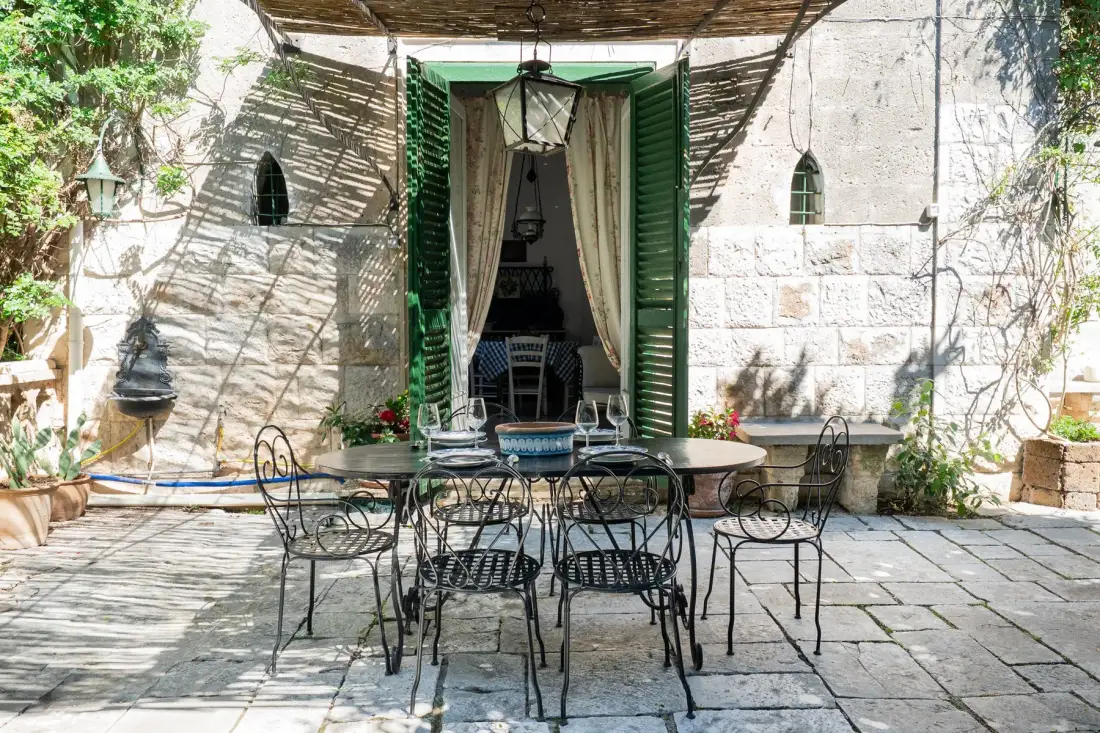 Un comedor en un patio de piedra con mesas y sillas de metal bajo una cubierta.