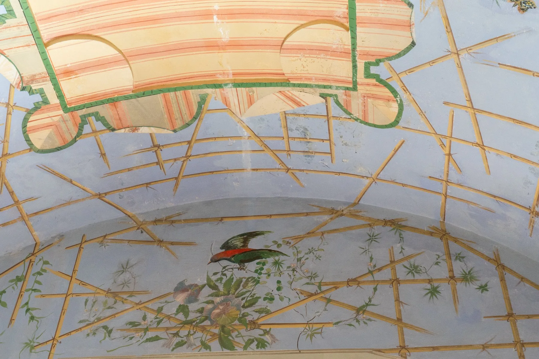 Un mural pintado en el techo muestra aves entre ramas frondosas sobre un fondo azul pálido.