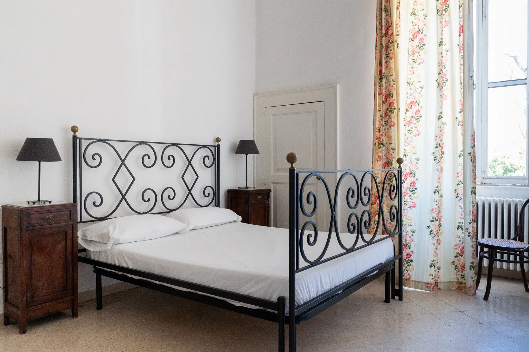 Un dormitorio con una cama de metal, mesas de noche y cortinas florales.