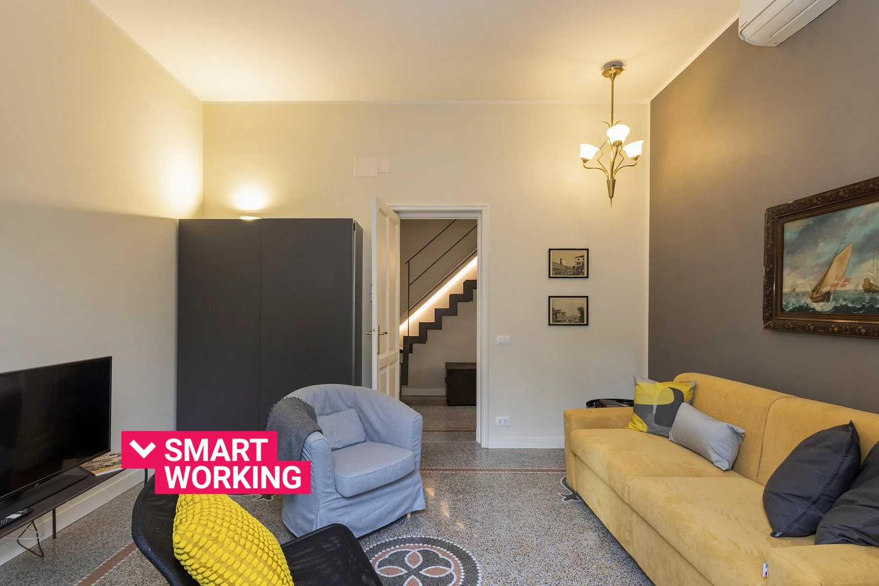 Una sala de estar con asientos, un televisor y una escalera visible a través de la puerta.