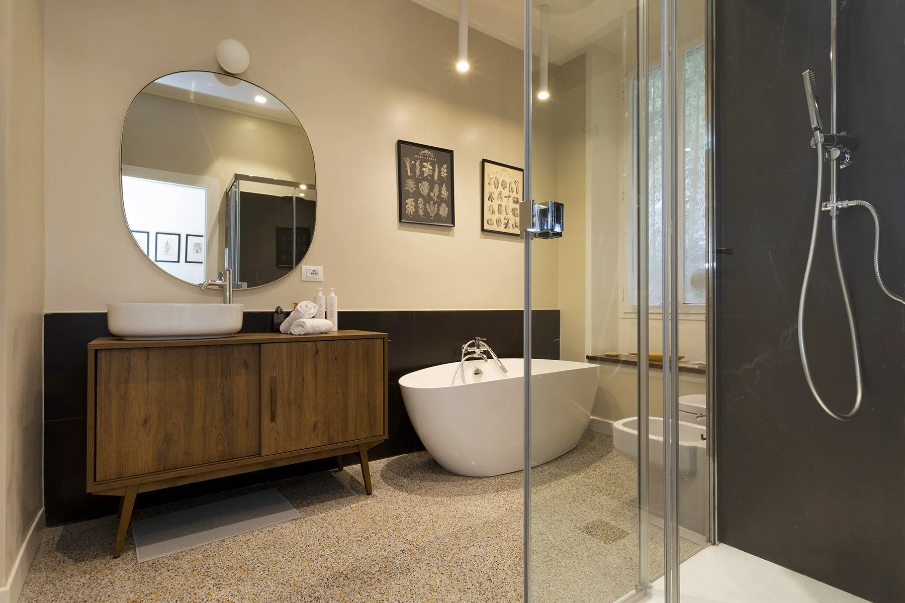 Un baño con bañera exenta, mueble de madera y ducha de cristal.