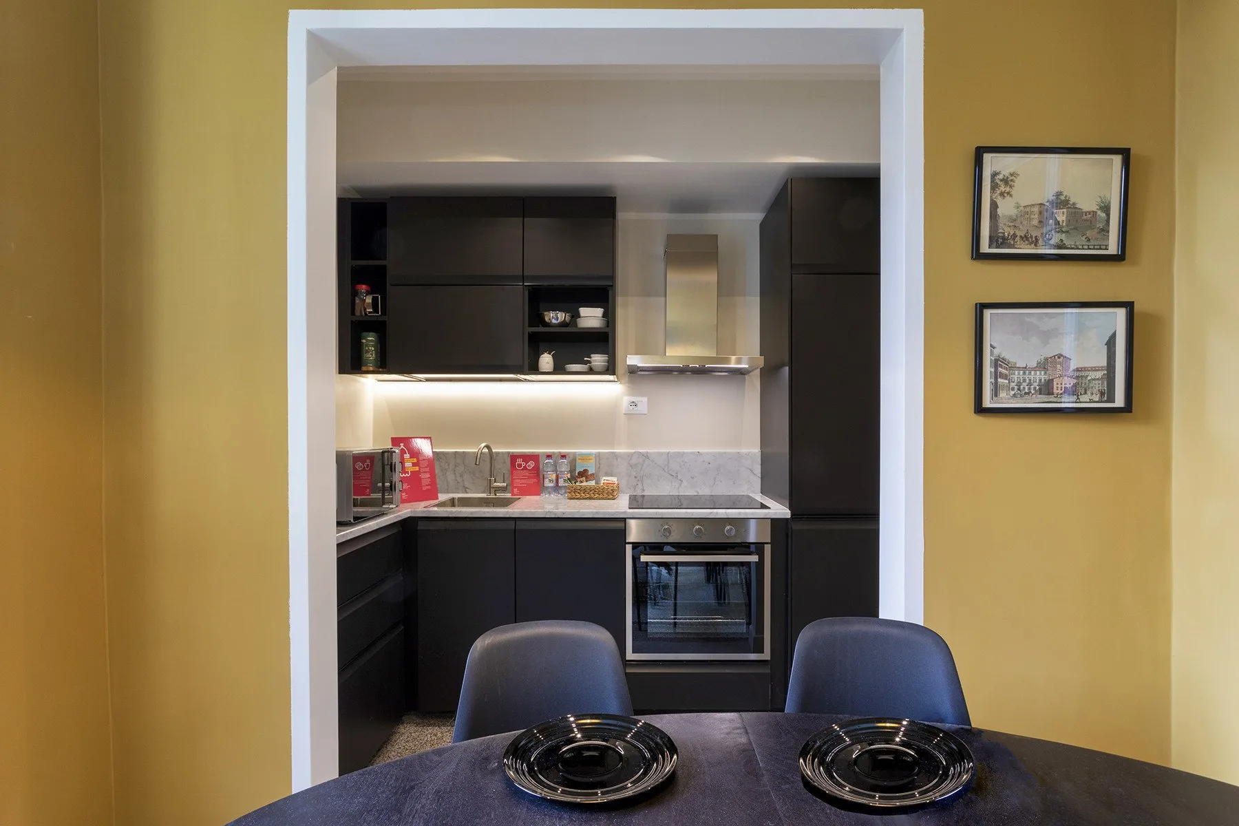 Una mesa de comedor con cubiertos está frente a una cocina moderna.