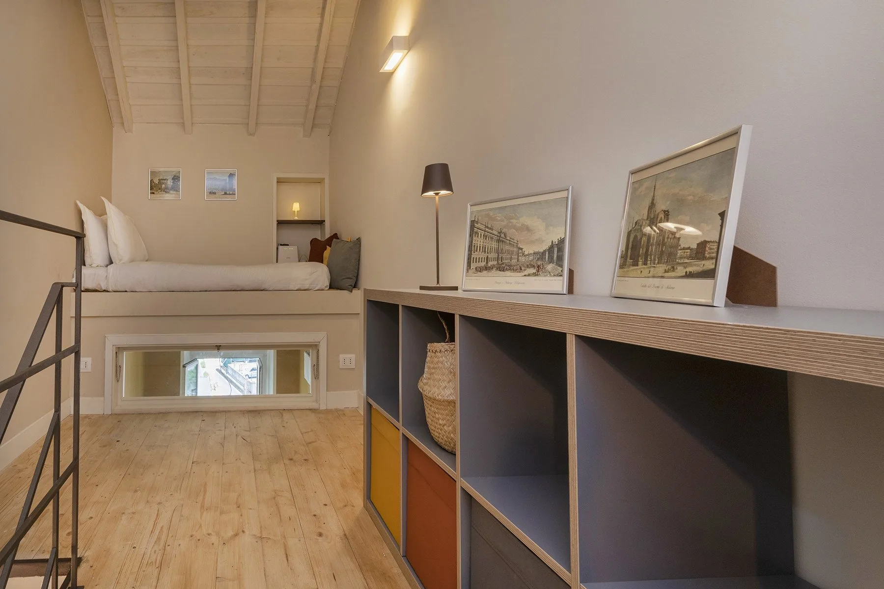 Un dormitorio tipo loft con cama elevada, estantes abiertos y cuadros enmarcados.