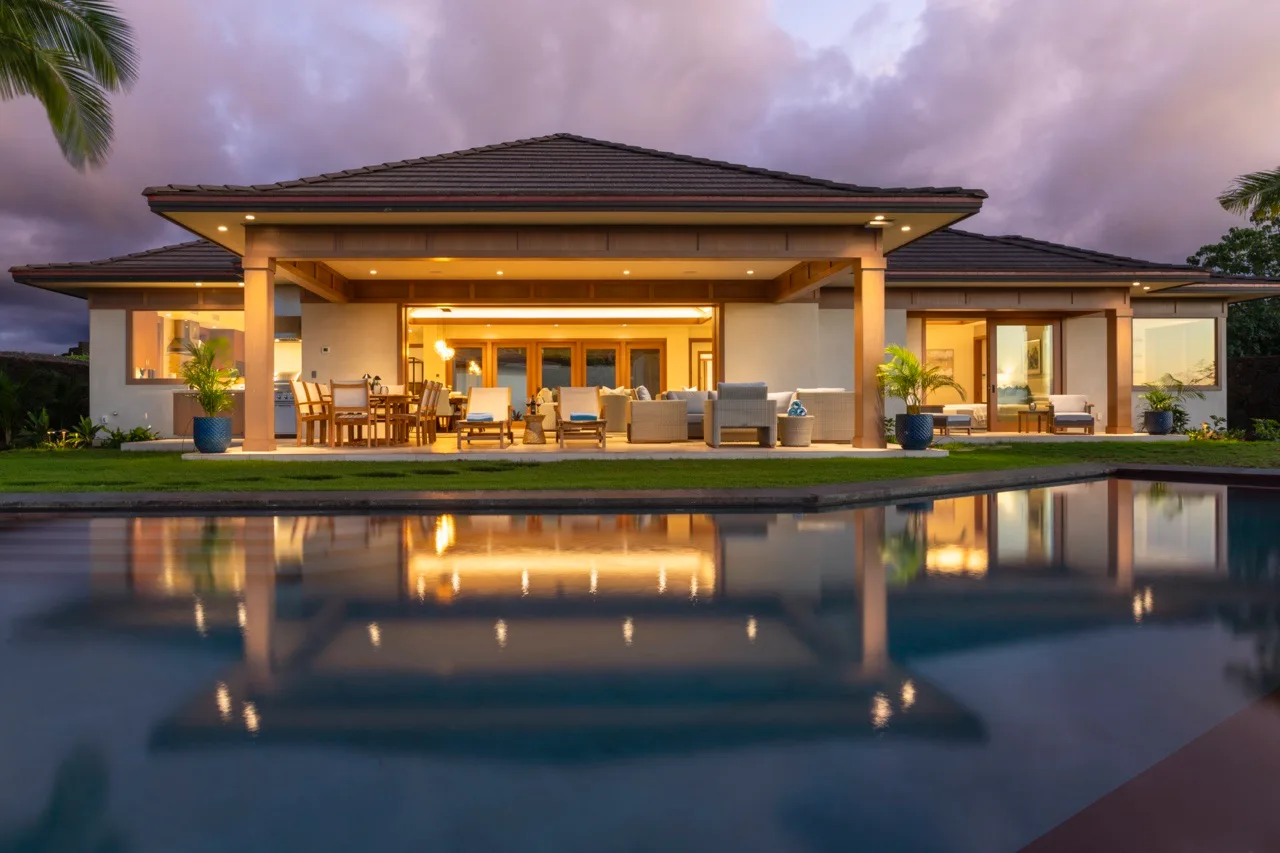 Una casa moderna da a un patio junto a una piscina al anochecer.
