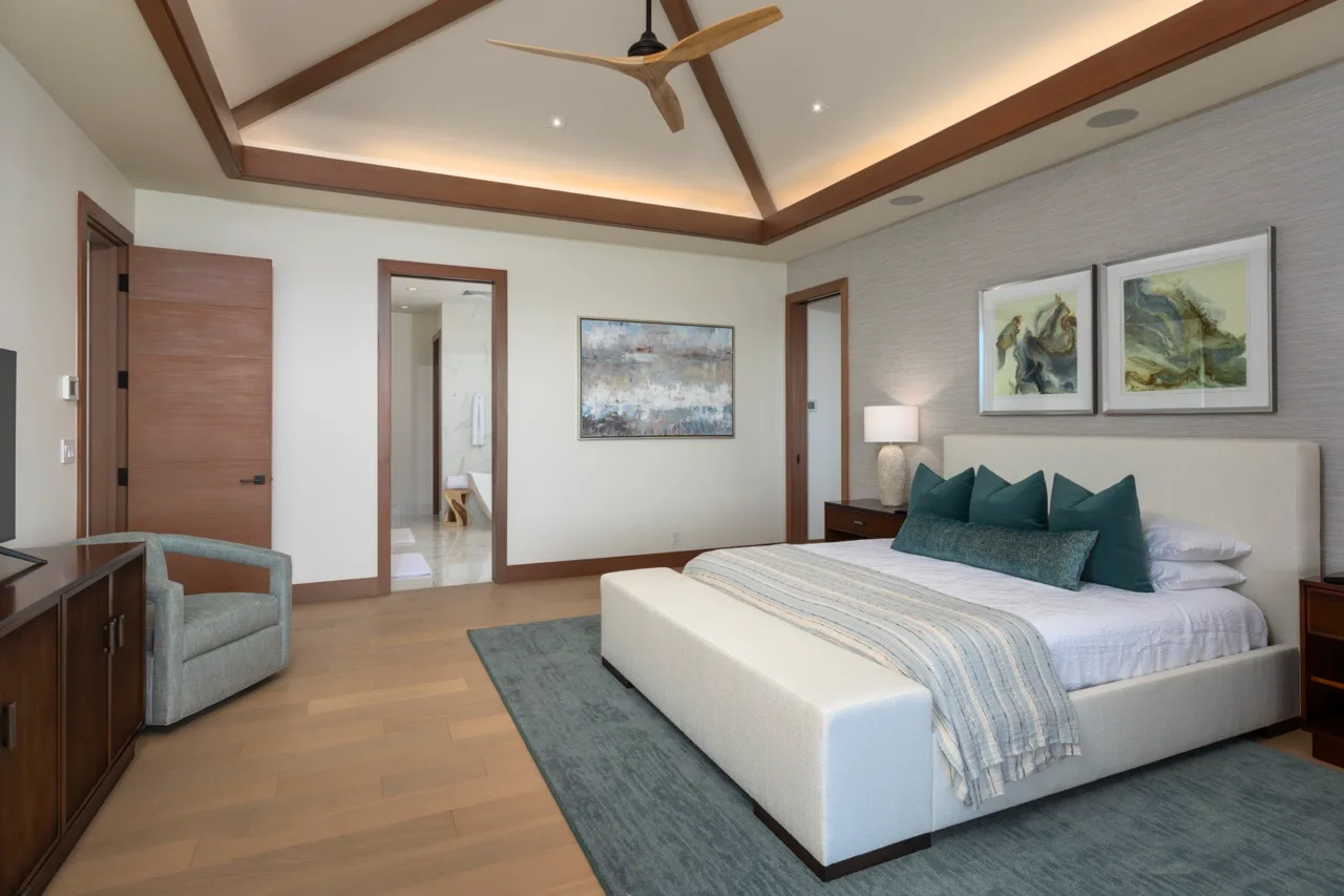 Un dormitorio con una cama, cojines verde azulado y vigas de madera expuestas en el techo.