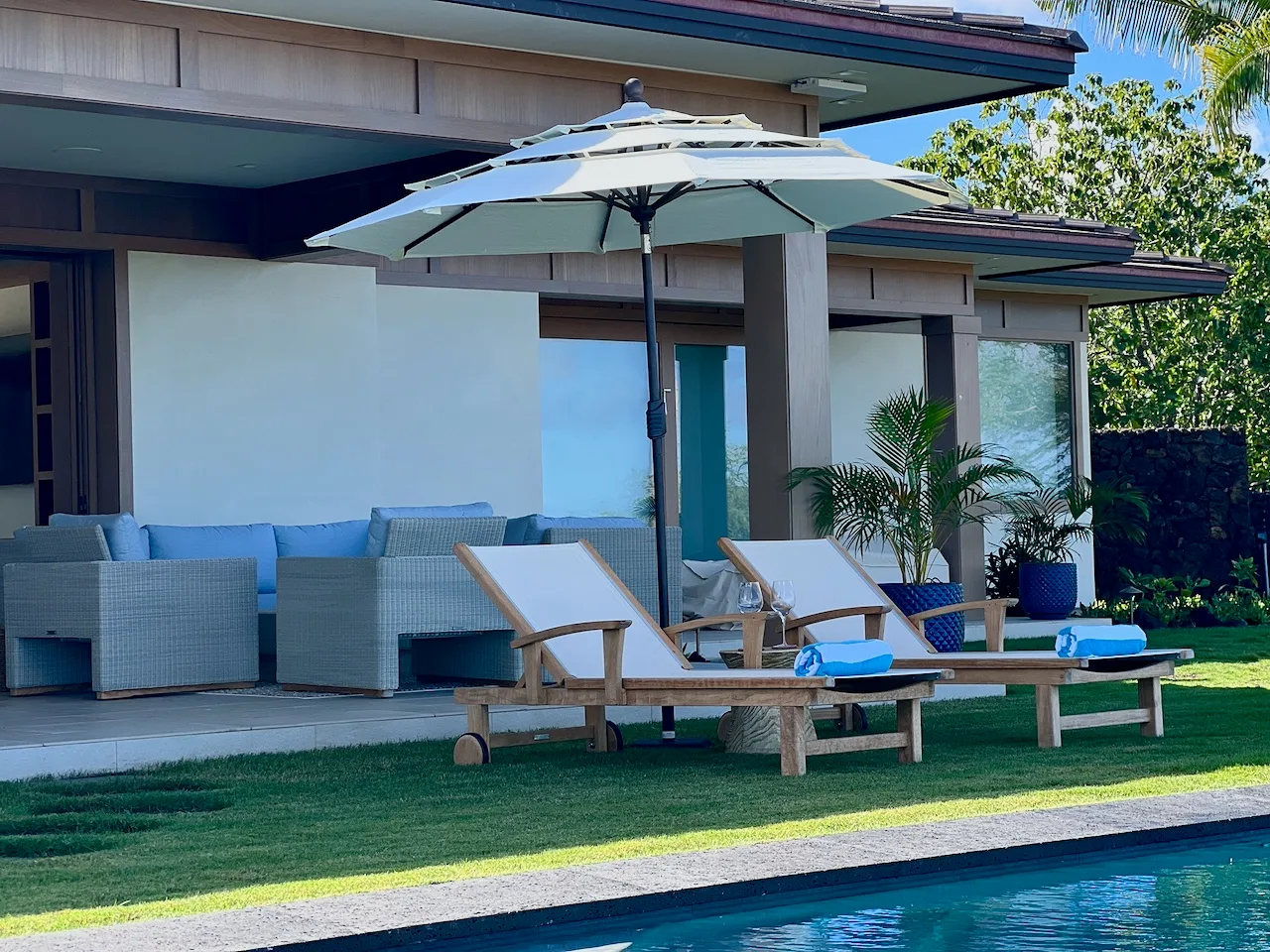 Un patio junto a la piscina con asientos, una sombrilla y césped.