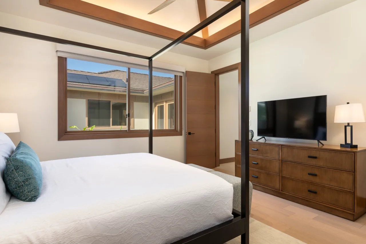 Un dormitorio con una cama blanca, una cómoda de madera y un televisor.