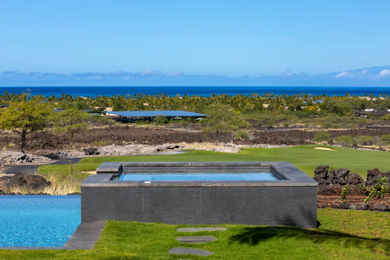 Una piscina da a un césped verde, vegetación costera y el océano.