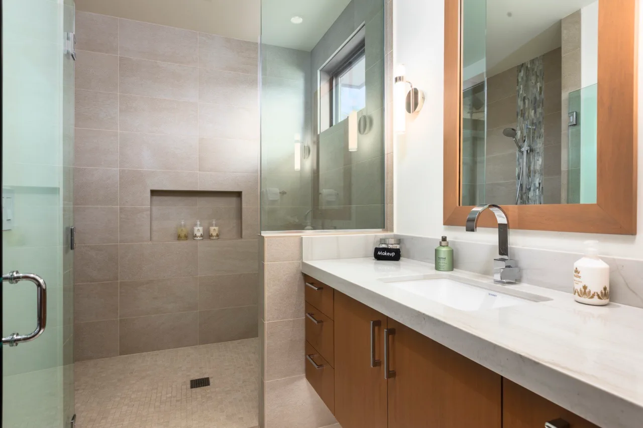 Un baño revestido de azulejos, con ducha de vidrio y un largo tocador bajo un espejo.