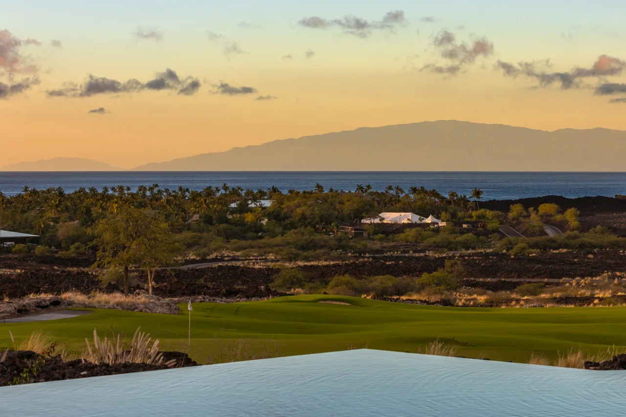 Un campo de golf y un paisaje costero se extienden hacia el océano bajo un cielo al atardecer.