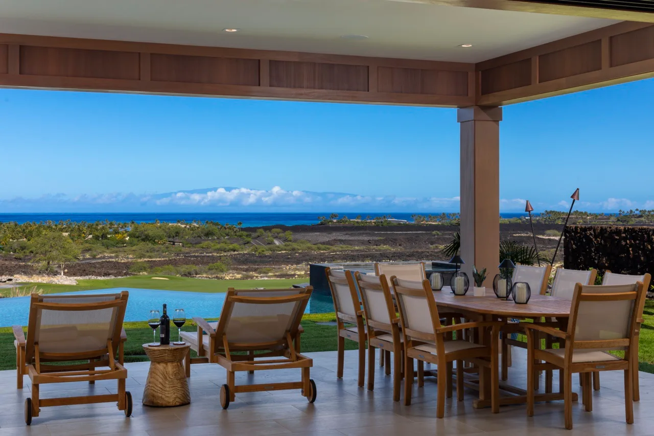 Una zona de comedor cubierta da a una piscina, un paisaje costero y el océano.