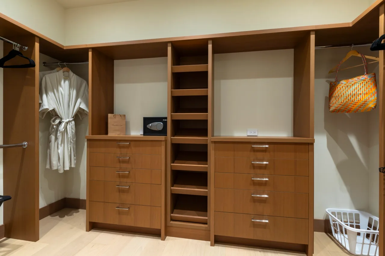 Un armario empotrado de madera con estantes abiertos, cajones y ropa colgada.