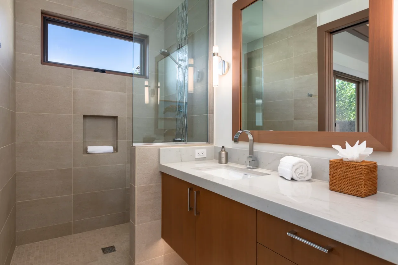 Un baño con azulejos, una ducha de vidrio y un largo tocador con lavabo.