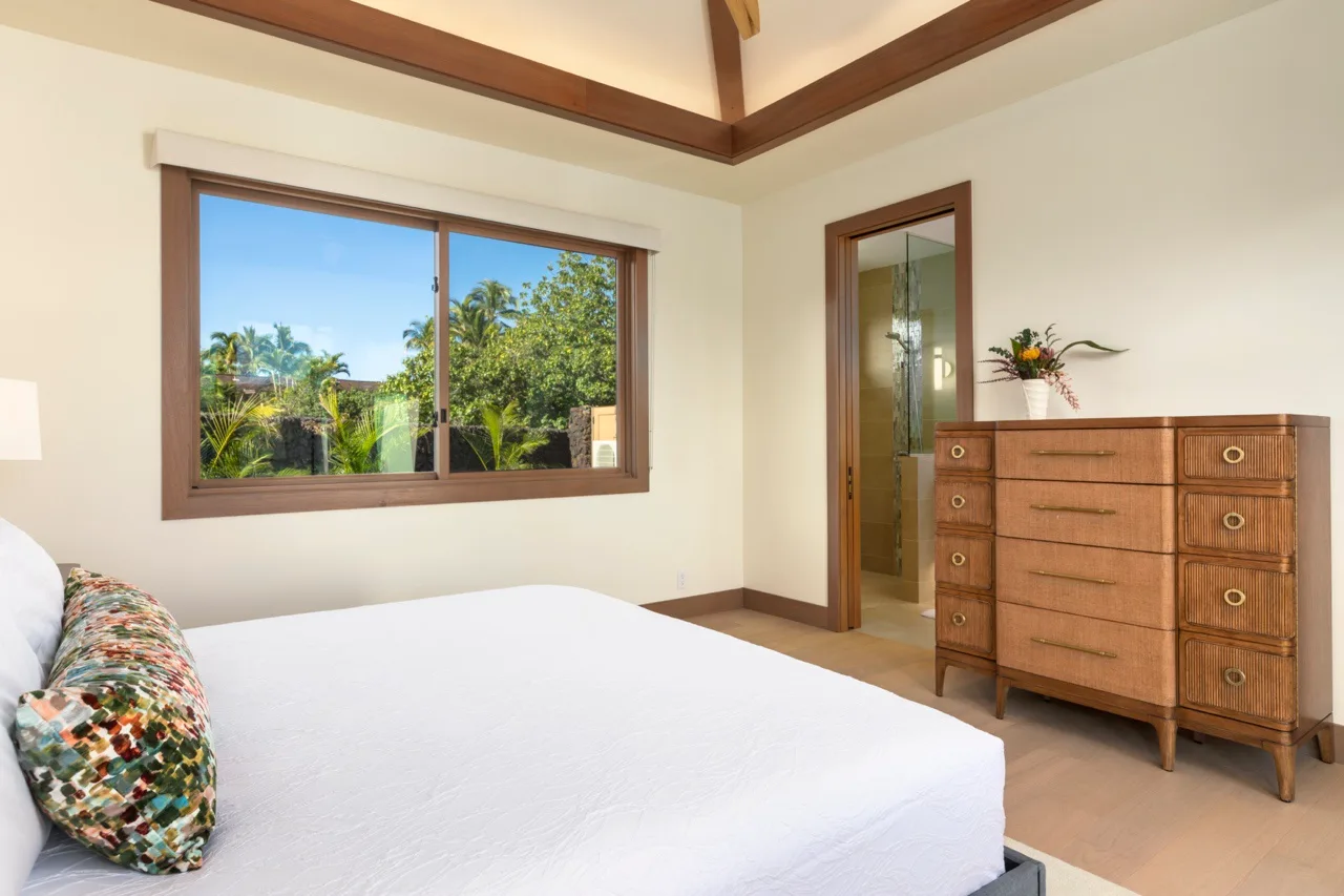 Un dormitorio con una cama, una ventana con vistas a la vegetación y una cómoda de madera.
