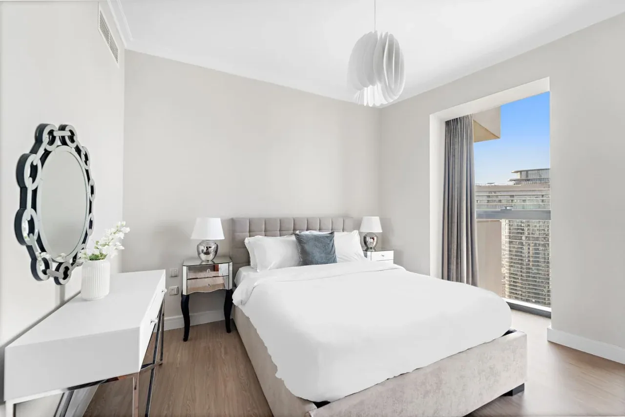 Un dormitorio luminoso con una cama tendida y una ventana grande.