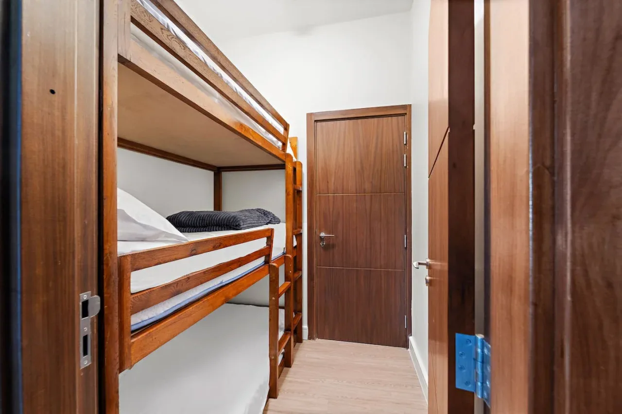 Un dormitorio estrecho con literas de madera y una puerta cerrada.