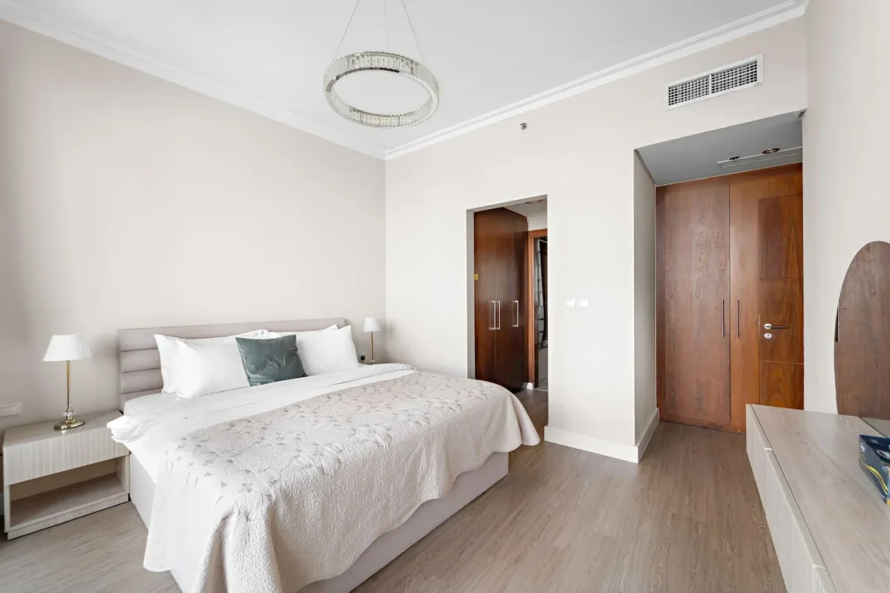 Un dormitorio luminoso con una cama bien tendida y un armario de acabado en madera.