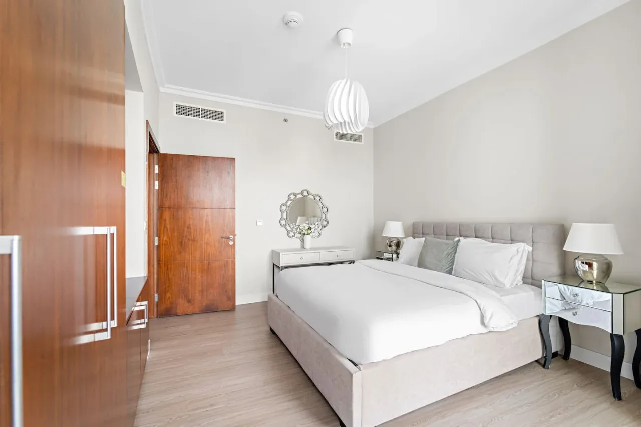 Un dormitorio luminoso con una cama, mesitas de noche y una puerta de madera.