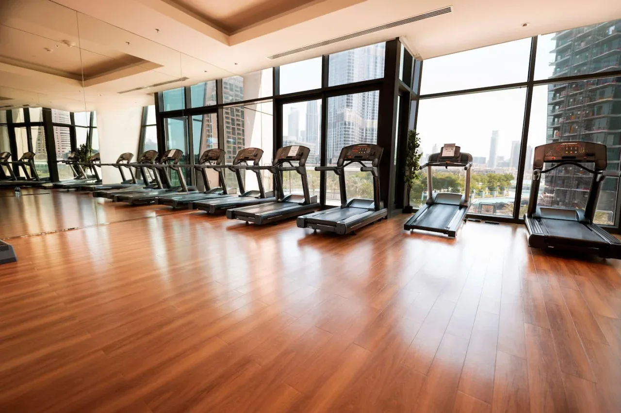 Un gimnasio con cintas de correr junto a grandes ventanales.