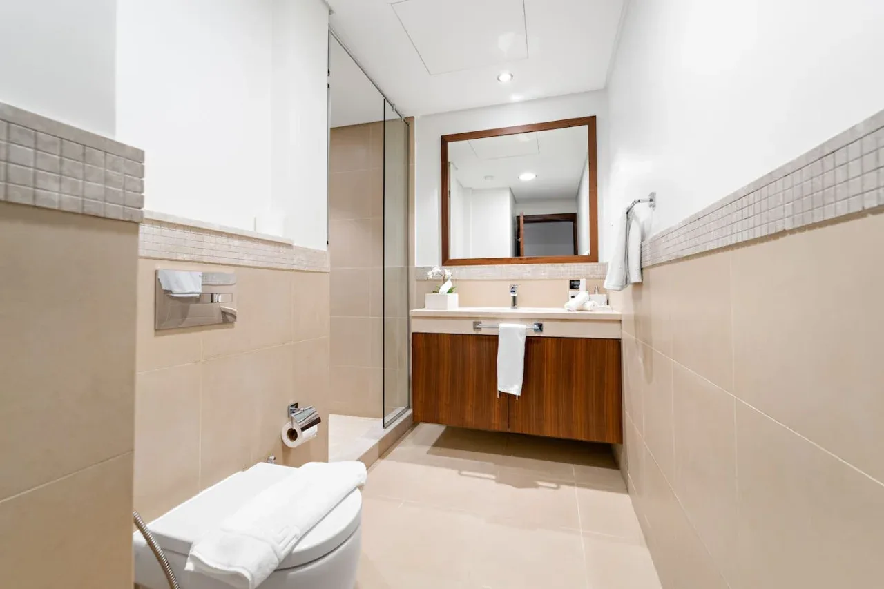 Un baño luminoso con lavabo, espejo, inodoro y panel de ducha de vidrio.
