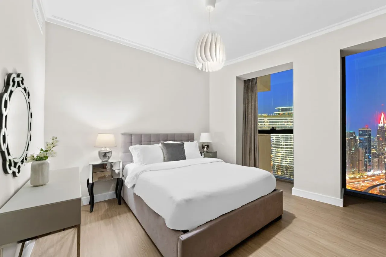 Un dormitorio luminoso con una cama bien hecha y grandes ventanales con vistas a la ciudad.