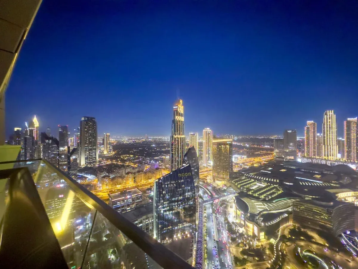 Vista nocturna del horizonte urbano desde un balcón elevado, con edificios y vías iluminados.