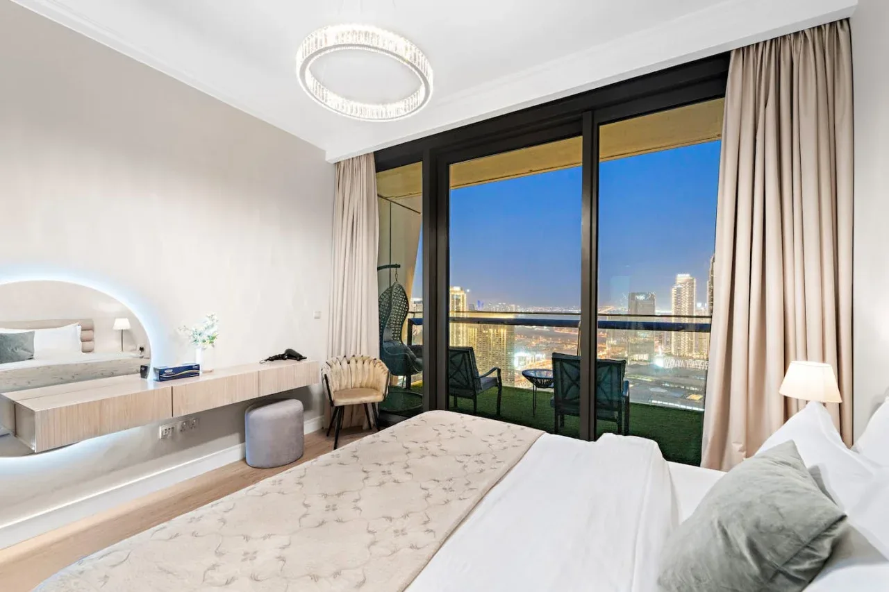 Un dormitorio con una cama junto a ventanales que dan a un horizonte urbano.