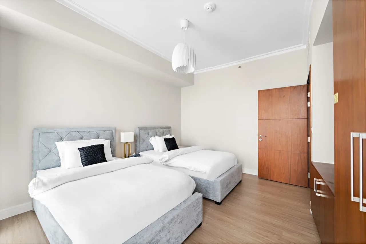 Un dormitorio luminoso con dos camas, ropa de cama blanca y paredes claras.