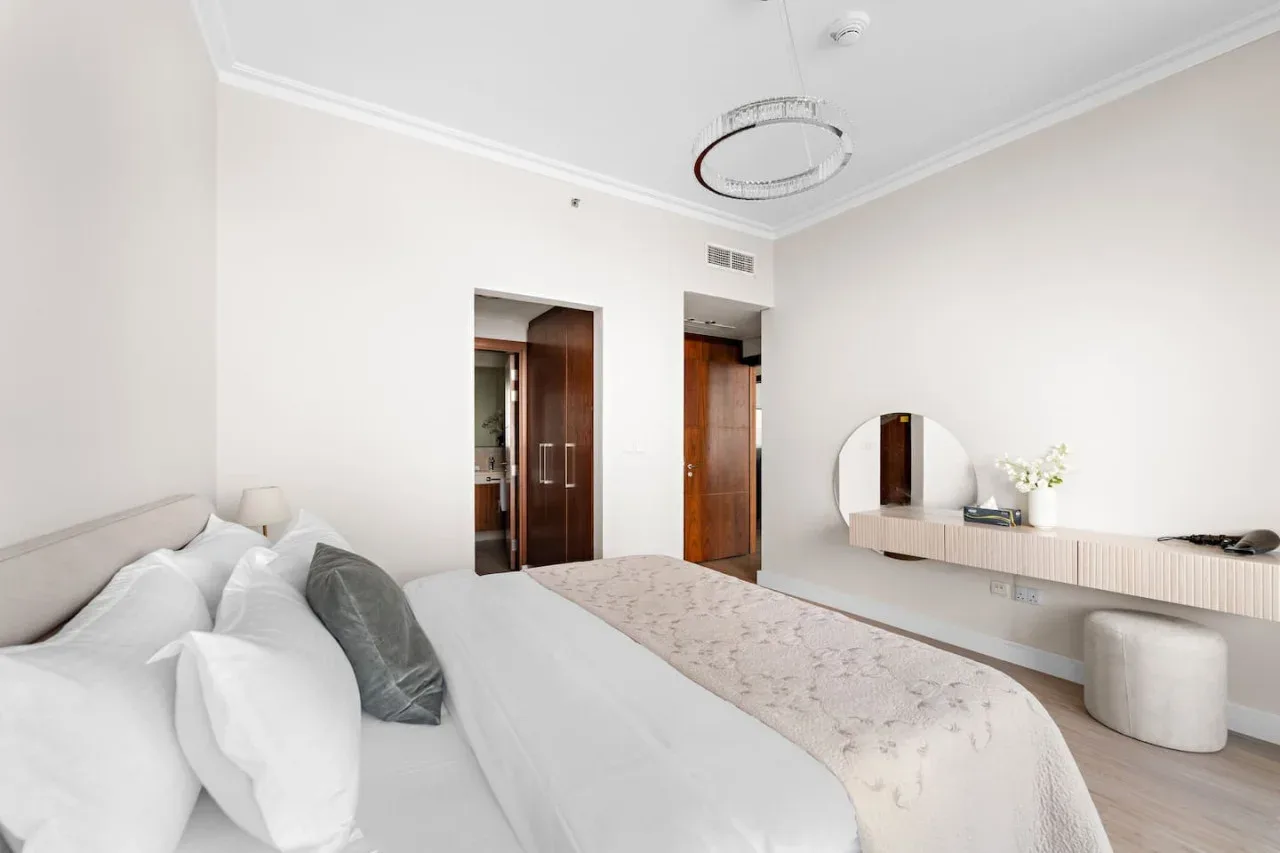 Un dormitorio luminoso con una cama, lámparas de noche y un tocador mural.