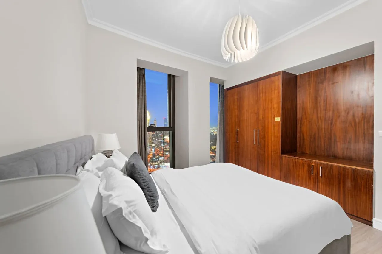 Un dormitorio con una cama blanca, armarios de madera y ventanas altas.