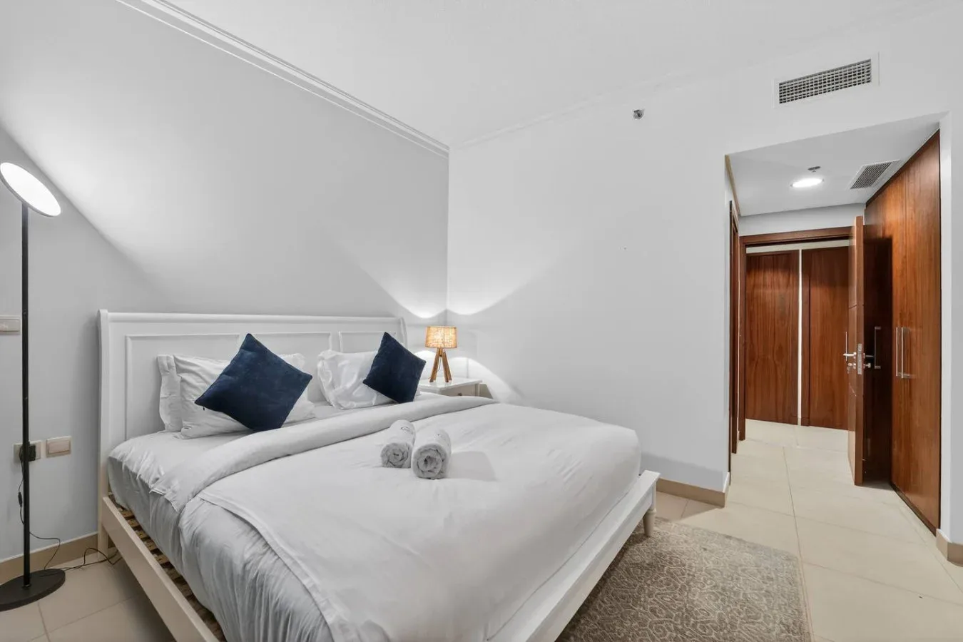 A bright bedroom with a large bed, white linens, and dark accent pillows.