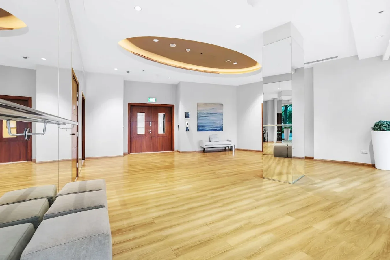 A bright lobby has polished wood flooring, mirrored walls, and seating.