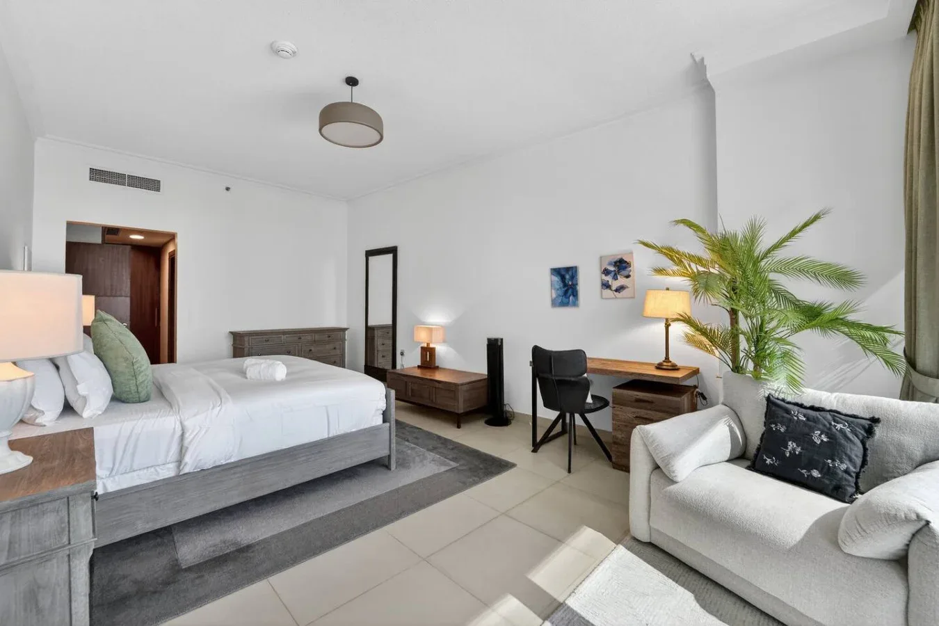 A bright bedroom with a bed, desk, and seating area.