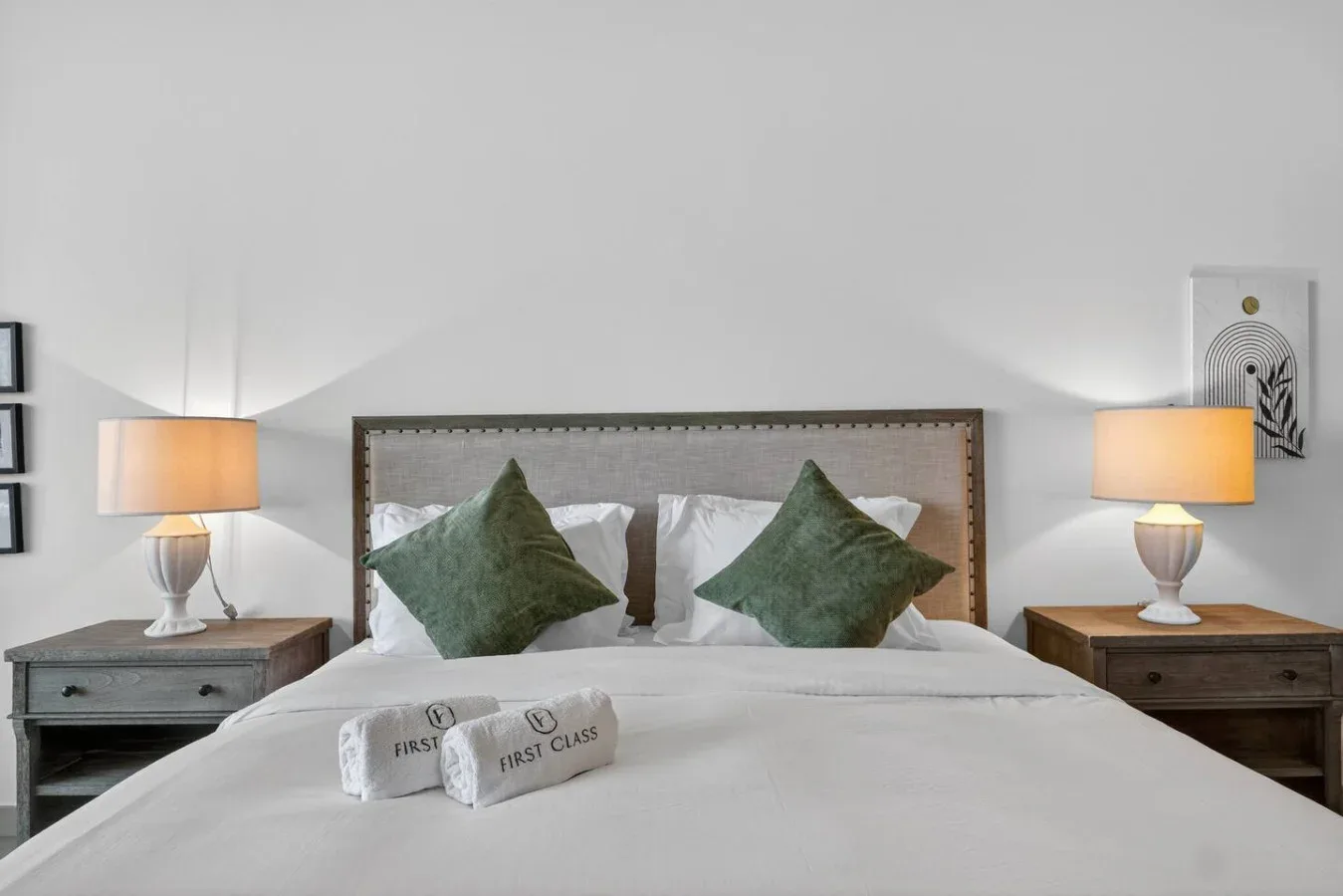 A neatly made bedroom bed with green pillows and matching bedside lamps.