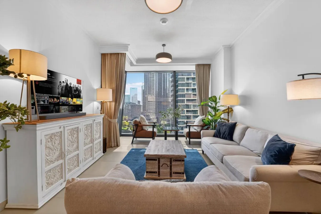 A bright living room with seating arranged around a coffee table and large windows.