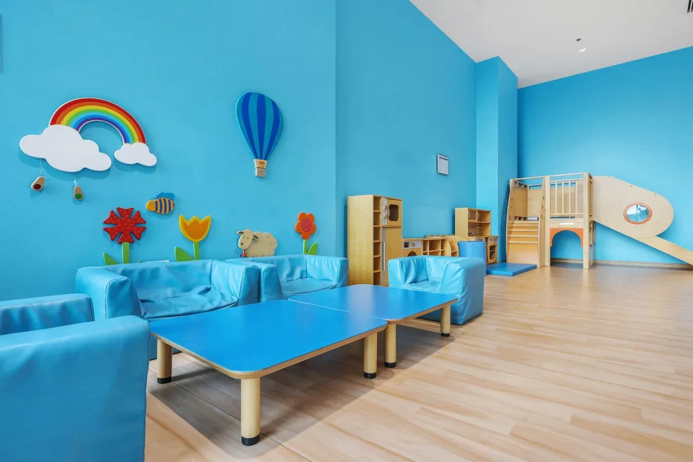 A brightly colored indoor playroom with low tables and a small climbing structure.