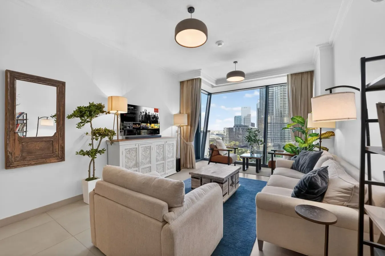 A bright living room with seating, a television, and large windows overlooking the city.