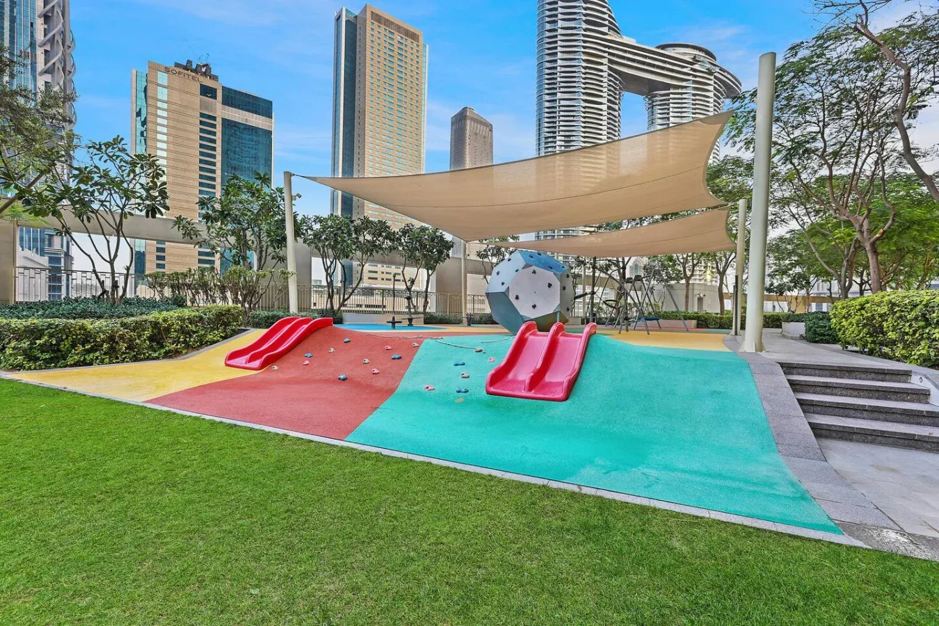 A colorful outdoor playground has slides beneath a broad shade canopy.