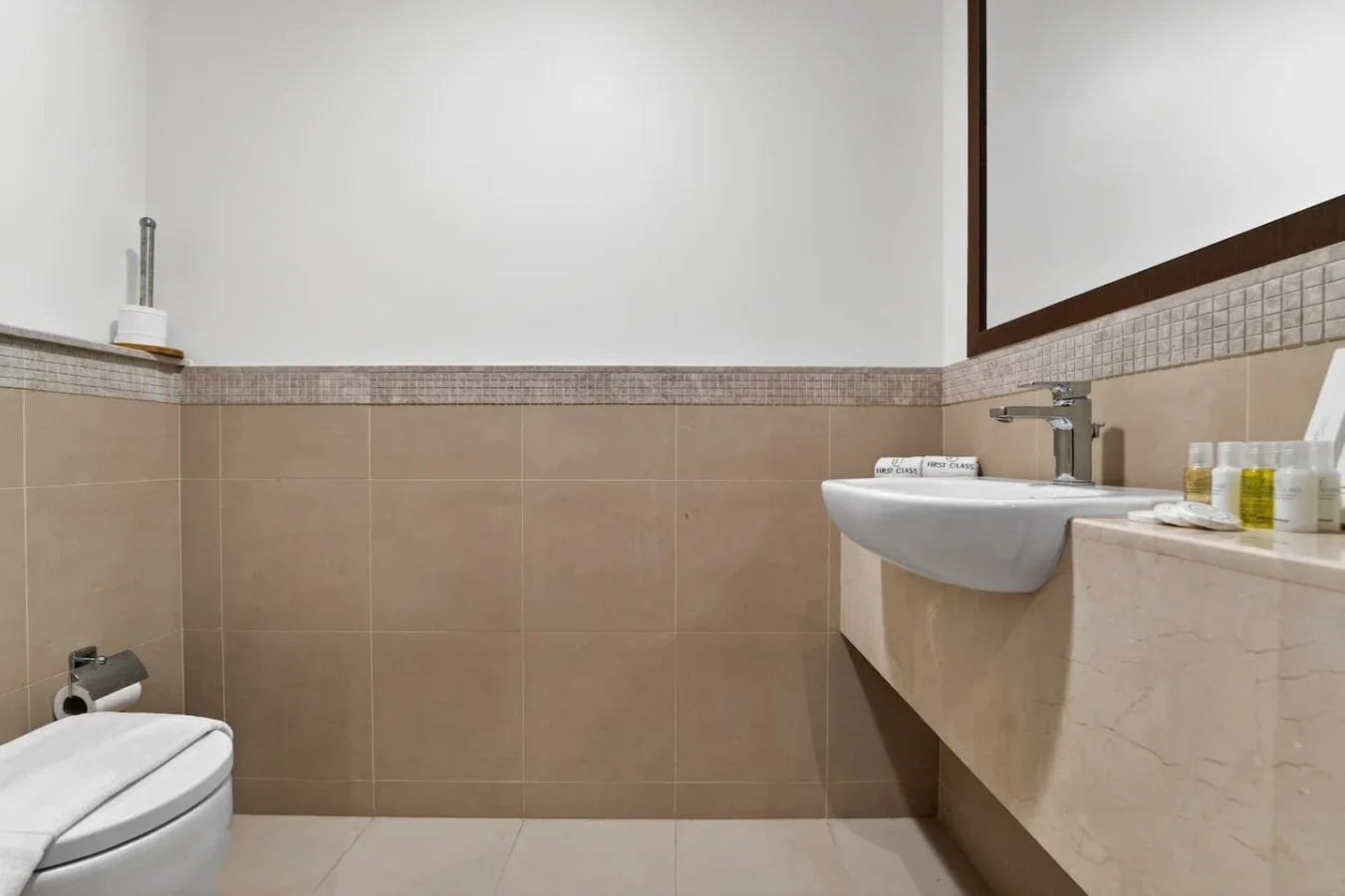 A tiled bathroom with a sink, toilet, and toiletries on the counter.