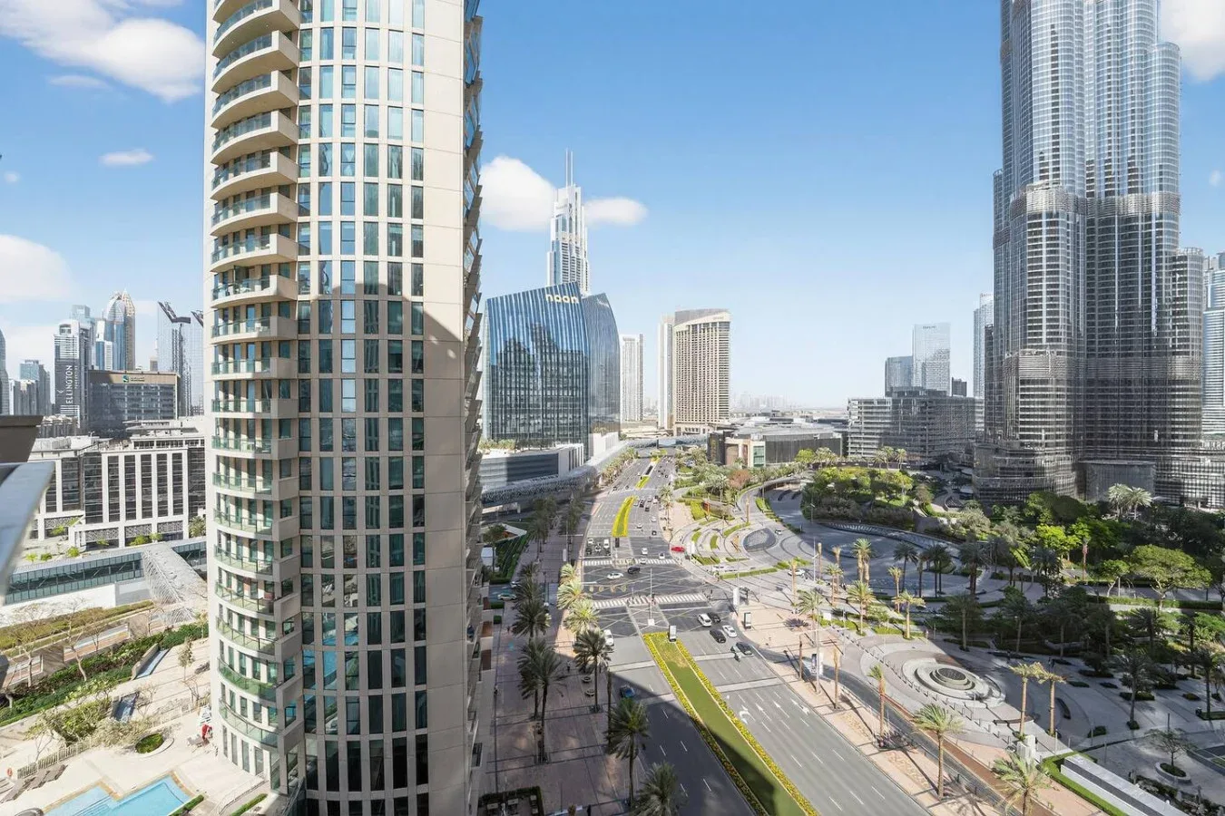 A city skyline overlooks a broad road and landscaped urban plaza.