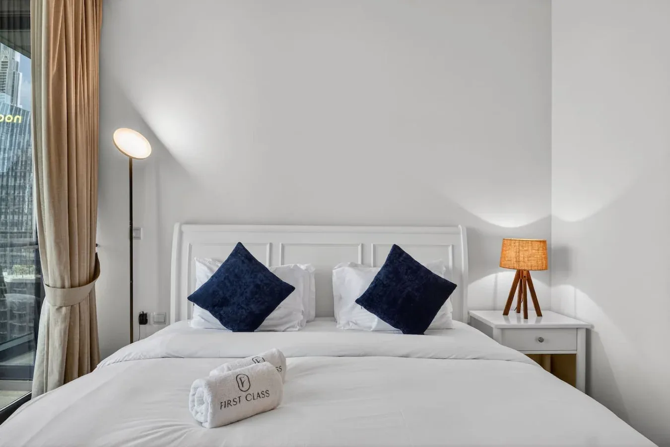 A bright bedroom with a neatly made bed and dark accent pillows.