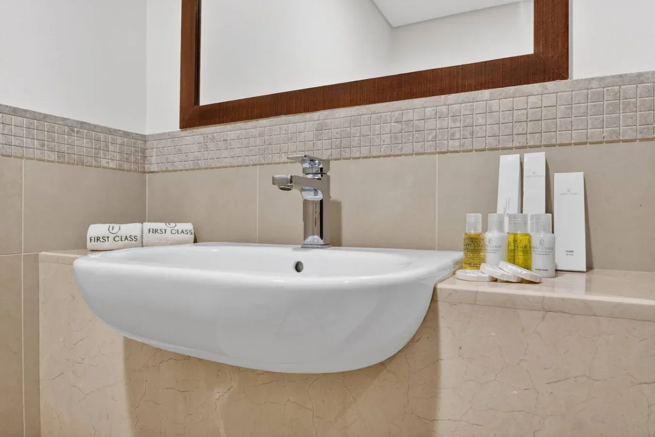 A bathroom sink sits beneath a large mirror, with toiletries arranged nearby.