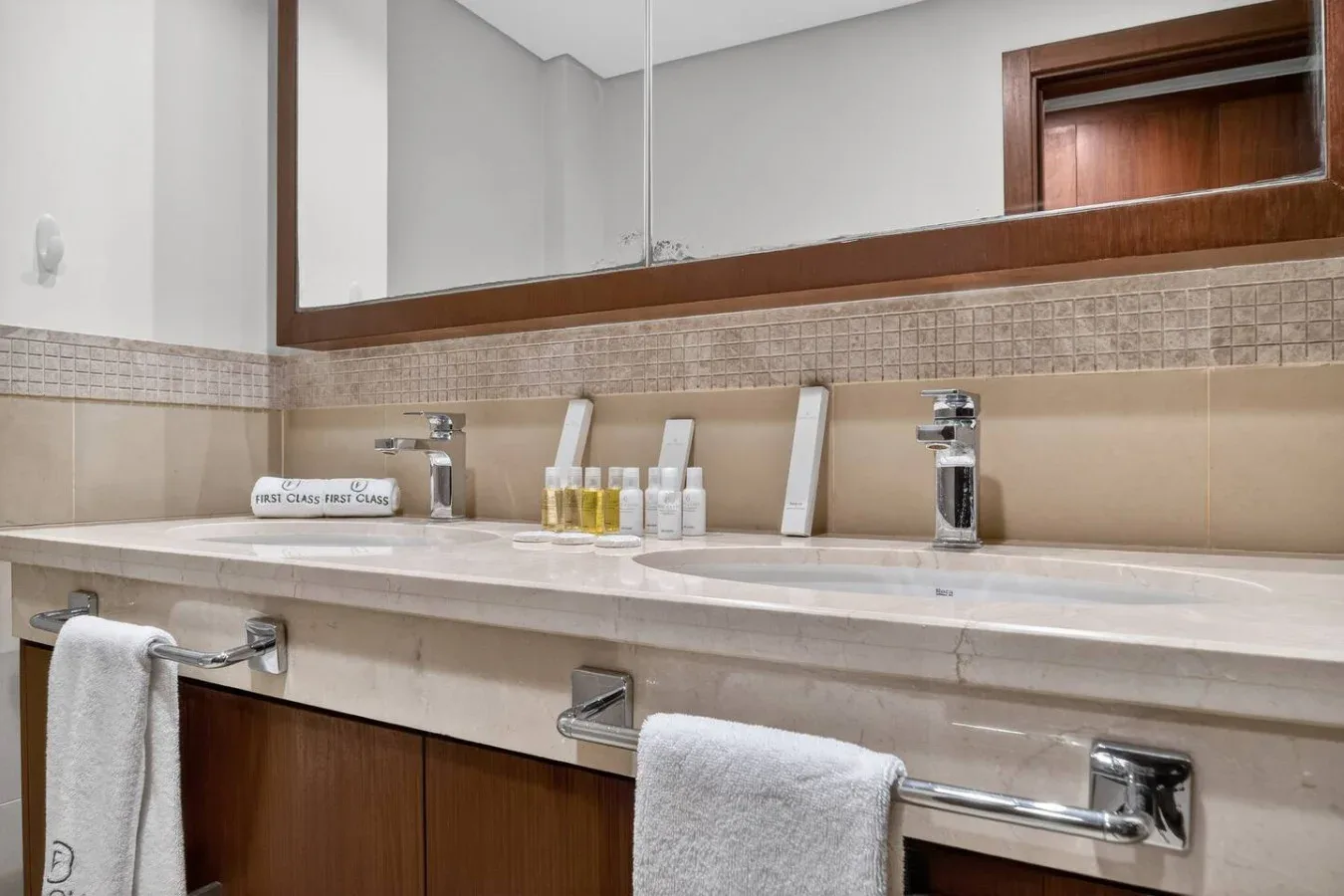 A bathroom vanity with a wide mirror, two sinks, and folded towels.