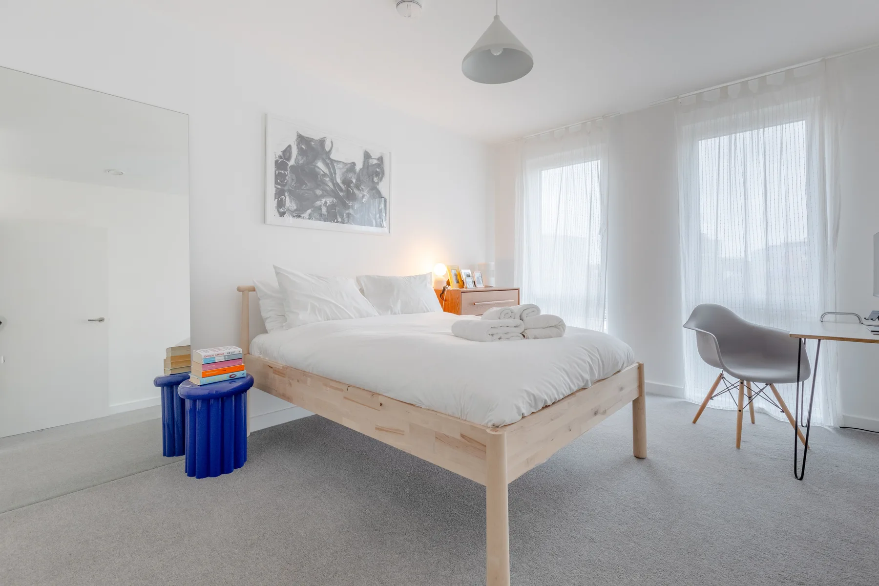 A bright bedroom with a bed and a desk beside tall windows.