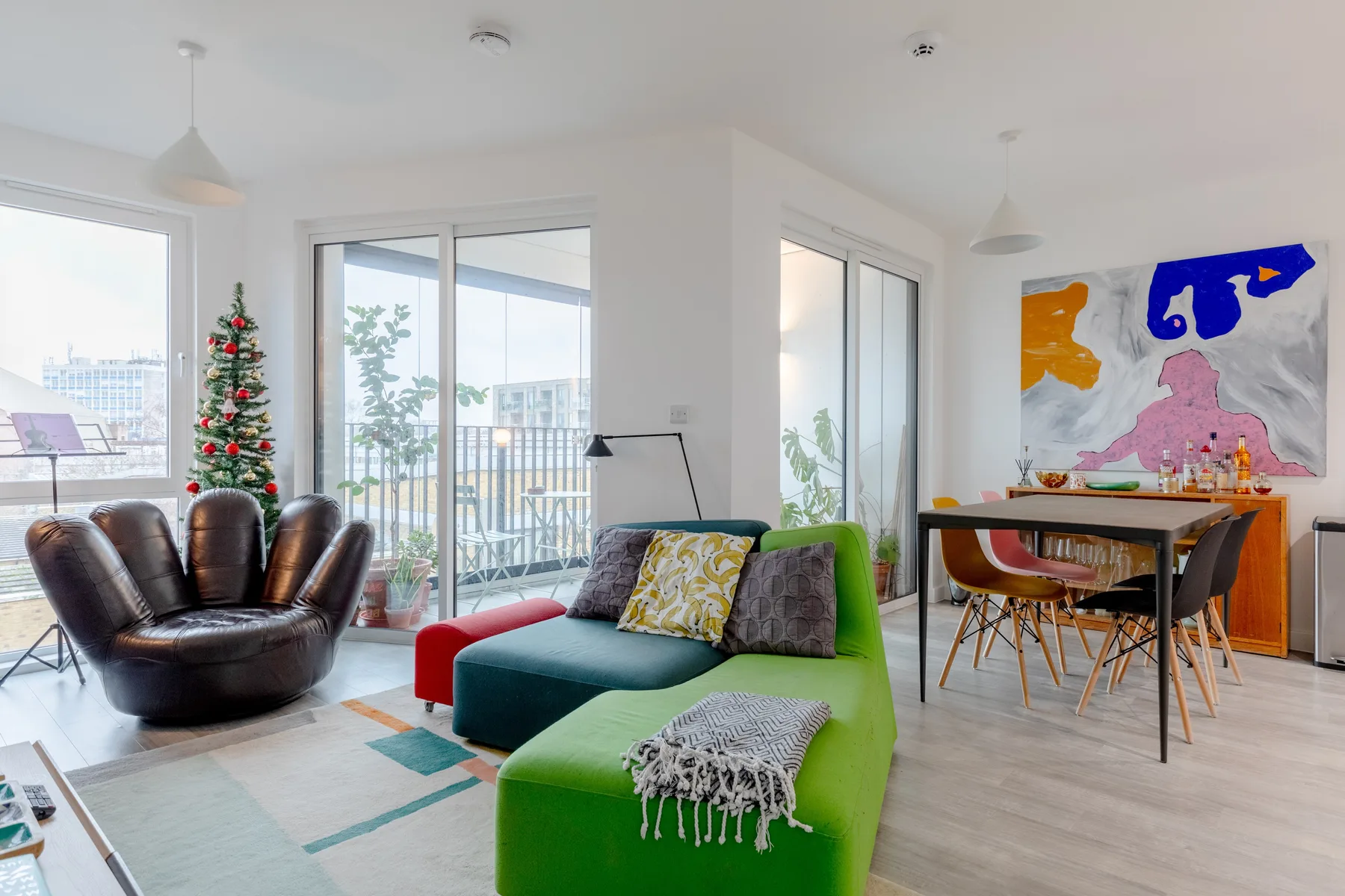 A bright living and dining area with colorful seating and a table by the windows.