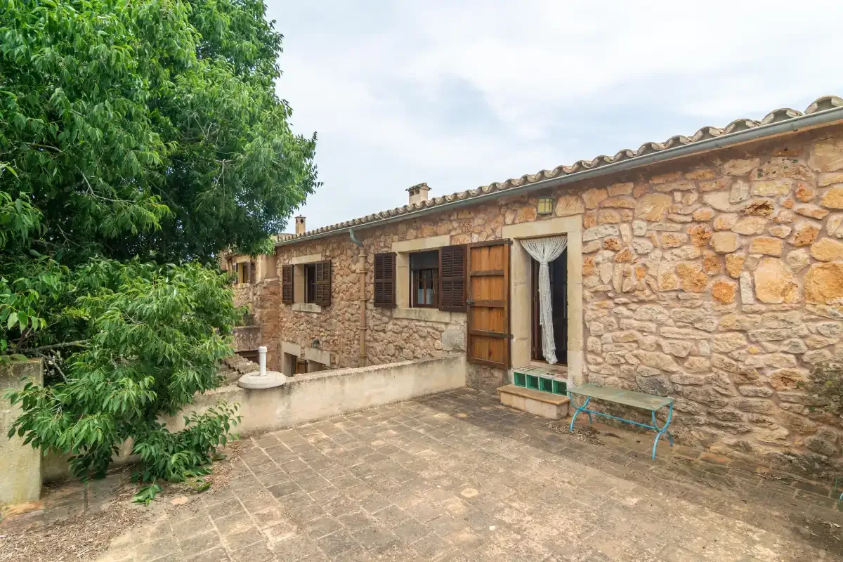 Stone house exterior with an open wooden door facing a paved patio.