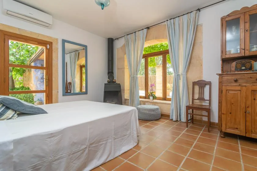 A bright bedroom with a bed, curtained windows, and wooden furnishings.