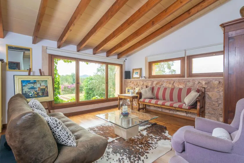 A living room with seating around a glass coffee table and large windows.